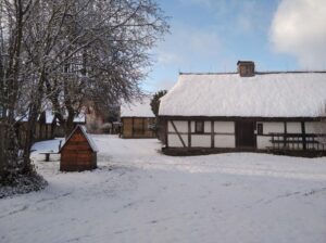 Skansen w Nadolu pokryty śniegiem. W centralnym miejscu zdjęcia widać chatę przykrytą śniegiem. Po lewej stronie widać ośnieżone drzewa